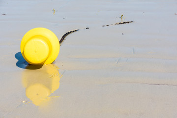 Close-up view of a large yellow buoy and its anchorage chain, used as a launching channel marker, lying on the wet sand on the beach in Penvenan, Brittany, France, under a bright sunshine.
