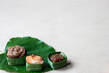Thai sweets in banana leaves that are arranged on leaf with brown paper background.