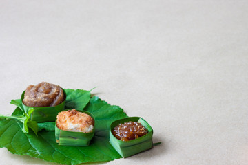 Thai sweets in banana leaves that are arranged on leaf with brown paper background.