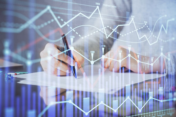 Hand taking notes in notepad. Forex chart holograms in front. Concept of research. Multi exposure