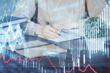 Forex graph on hand taking notes background. Concept of research. Double exposure