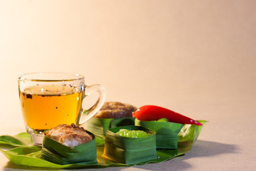 Thai sweets in banana leaves and cup of tea that are arranged on leaf with brown paper background.