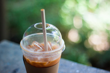 Cold milk tea in plastic glasses on wood table with blur tree background.