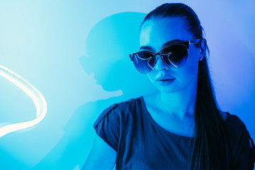 Night portrait of a young beautiful girl in sunglasses in blue neon light.