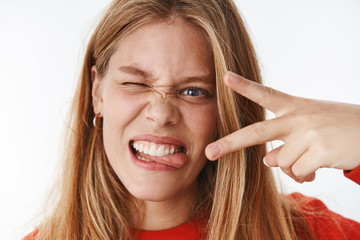 Headshot of funny emotive and charismatic young carefree girl making faces sticking out tongue...