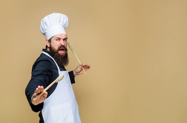 Handsome chef cook with kitchen utensils. Chief man in cook uniform holds wooden kitchen cooking tools. Bearded man preparing to cook food. Bearded cook with wooden spoon and spatula in hand.