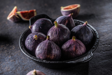 A few figs in a black bowl on an dark concrete table
