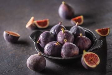 A few figs in a black bowl on an dark concrete table
