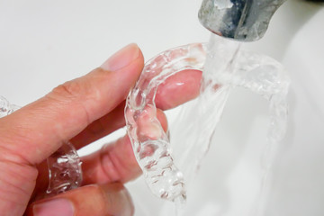 hand holding clear plastic retainer teeth that isolated on blue sky background. it's an equipment for orthodontist give the patient to orthodontic surgery in dental clinic or hospital