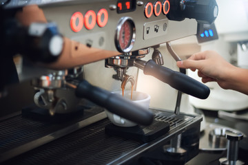 Barista making coffee with coffee machine preparing fresh coffee and pouring into white cup in cafe