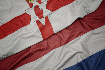 waving colorful flag of netherlands and national flag of northern ireland.