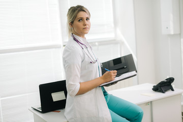 Portrait of woman doctor holding clipboard and pen. Doctor holding clipboard and pen against the background of a window