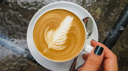 On glass table is white cup of cappuccino and latte art. Rosetta. Coffee shop and autumn. Morning...