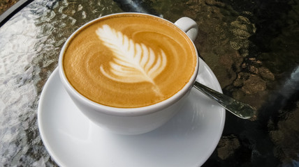 On glass table is white cup of cappuccino and latte art. Rosetta. Coffee shop and autumn. Morning coffee.