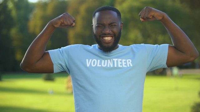 Excited african male volunteer t-shirt showing strength gesture, donation unity