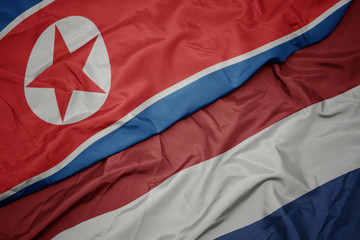 waving colorful flag of netherlands and national flag of north korea.