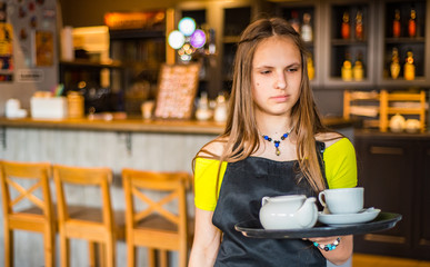 Portrait young waitress standing in cafe. girl the waiter holds in bunches a tray with utensils....