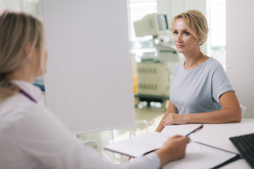 Fototapeta premium Doctor and oung woman patient sitting at the desk and talking in light clinic. Medicine and health care concept.