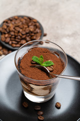 Portion of Classic tiramisu dessert in a glass cup on concrete background