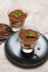Portion of Classic tiramisu dessert in a glass cup on concrete background