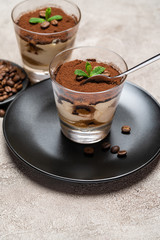 Portion of Classic tiramisu dessert in a glass cup on concrete background
