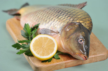 Uncooked carp with lemon and parsley on a wooden tray. Traditional dish for the christmas table. Light background. Close-up. 