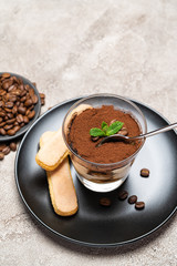 Portion of Classic tiramisu dessert in a glass cup on concrete background