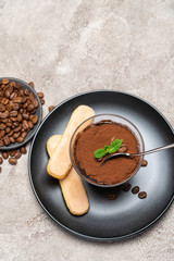 Portion of Classic tiramisu dessert in a glass cup on concrete background