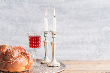 Shabbat or Sabbath kiddush ceremony composition with a traditional sweet fresh loaf of challah bread, glass of red kosher wine and candles on a vintage wood table with copy space
