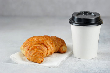 Coffee in a white paper cup and a croissant. Takeaway food and drink concept. Free space for text. Light background.
