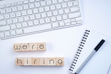 Wooden blocks with "We're hiring" text on keyboard on white background. Recruitment concept. Top view or flat lay.