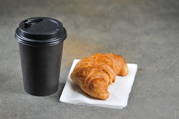 Coffee in a paper cup and a croissant. Takeaway food and drink concept. Free space for text. Dark background.