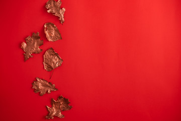 Rose gold colored fall leaves on red background from above. Autumnal minimalism flatlay. Copyspace for text