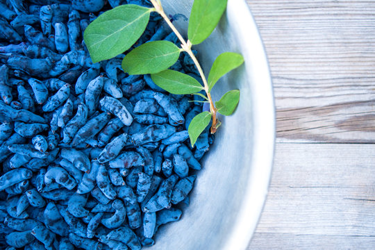 Bowl of honeysuckle berry or woodbine with green leaves on light coloured wooden background. Close up view.