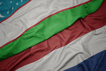 waving colorful flag of netherlands and national flag of uzbekistan.