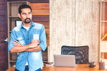 Portrait of handsome beard man holding a smartphone standing and looking outside the window, thinking of new work project.