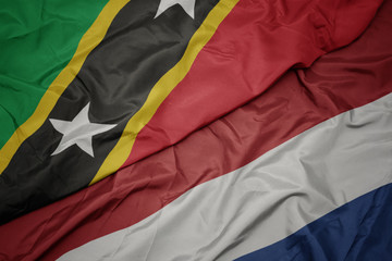 waving colorful flag of netherlands and national flag of saint kitts and nevis.