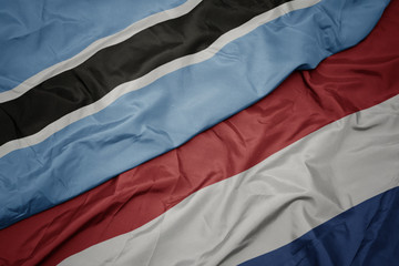 waving colorful flag of netherlands and national flag of botswana.