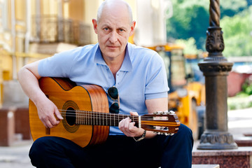 Gray-haired adult man in blue shirt plays guitar