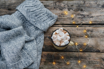 Fluffy white marshmallow in vintage bowl on old wooden table with sweater and Christmas lights.