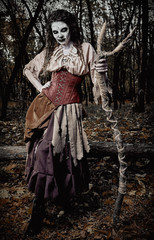 Fototapeta na wymiar Halloween theme: ugly creepy voodoo witch with staff. Portrait of evil hag in dark forest. Zombie woman (undead). Grunge texture effect