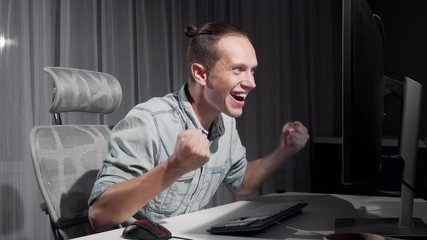 Happy man dancing in his chair in front of computer celebrating success. Cheerful male freelancer doing happy dance in front of his computer. Achievement, happiness concept