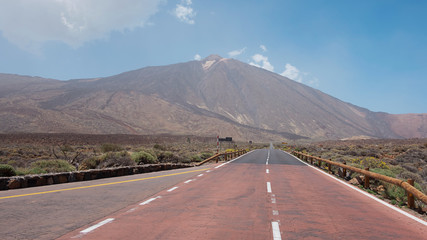 Naklejka premium Empty road passing through Teide National Park, with the volcano Pico del Teide in front, situated at high altitude and surrounded by the scarce endemic vegetation, in Tenerife, Canary Islands, Spain