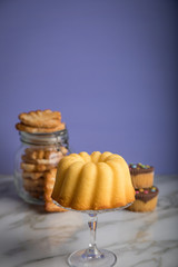 Gugelhupf Kuchen, Muffins und Italienische Blätterteig Fächer Kekse als Gebäck Auswahl Büffet auf Marmor Tisch und Lila Hintergrund