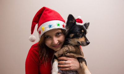 Happy girl in santa hat in red blouse with little black dog