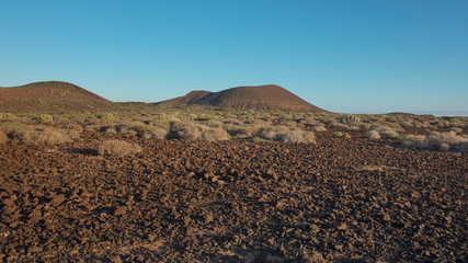 Arid volcanic landscape of Malpais de la Rasca, a natural reserve close to Palm-Mar town, inland views of the volcanic cones with basaltic structure, crumbling  lava rocks and flora and fauna habitats