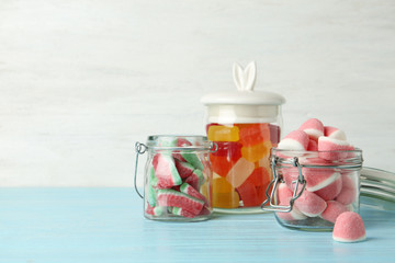 Glass jars with tasty jelly candies on blue wooden table against white background, space for text