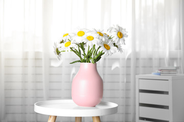 Vase with beautiful chamomile flowers on table in room