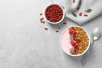 Smoothie bowl with goji berries and spoon on grey table, flat lay. Space for text