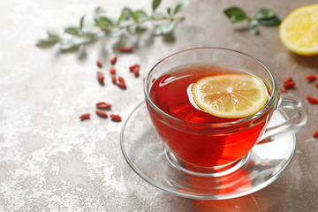 Glass cup of healthy goji tea with lemon on beige marble table. Space for text